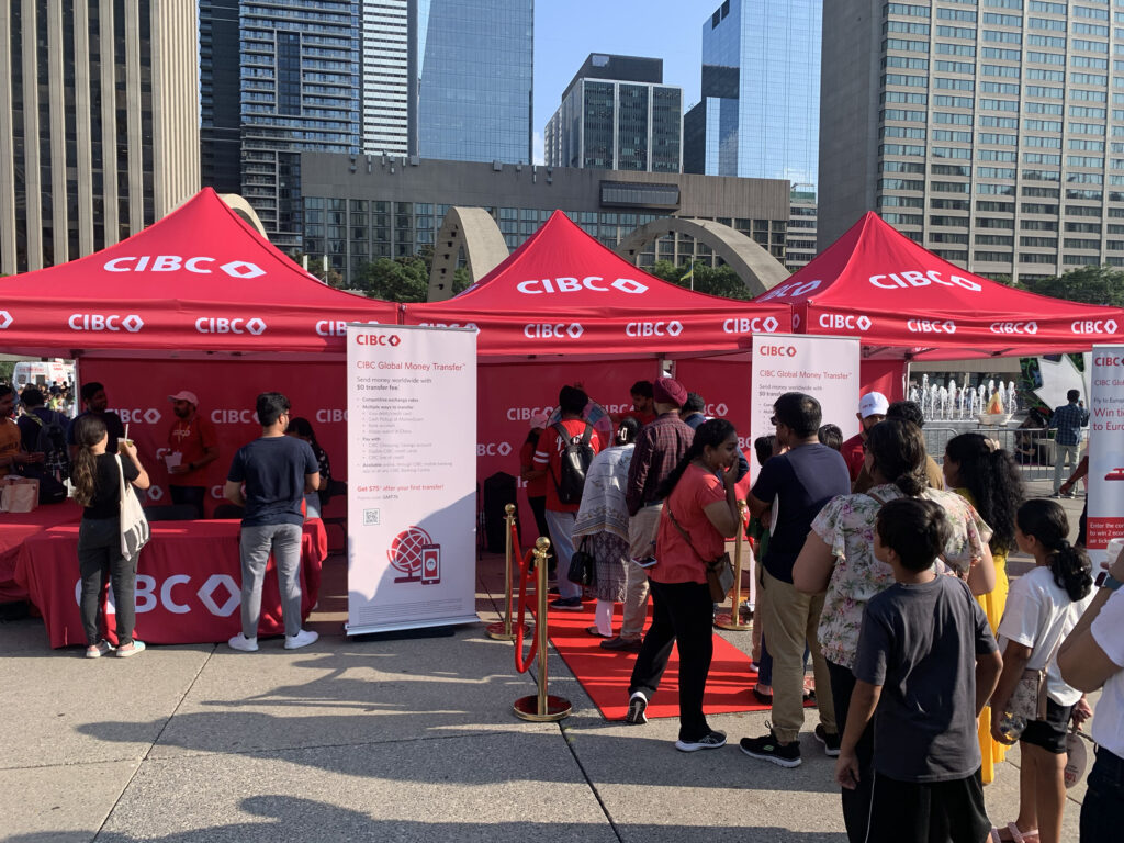 CIBC branded activation booth at a multicultural outdoor festival with red tents, promotional banners, and attendees lining up to engage with brand ambassadors in a downtown city setting.