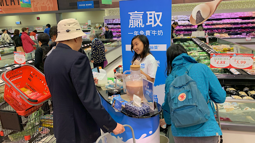 BC Milk brand ambassador offering product samples and engaging shoppers during in-store experiential marketing activation at grocery store.