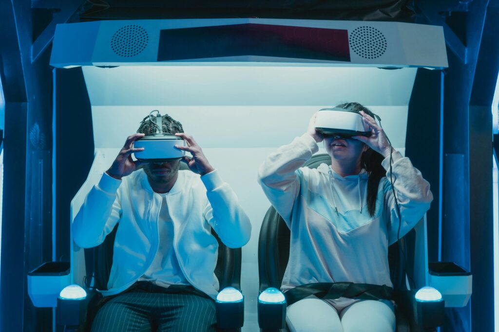 Two people seated in a futuristic setup using virtual reality headsets, adjusting the devices as they prepare for an immersive VR experience.